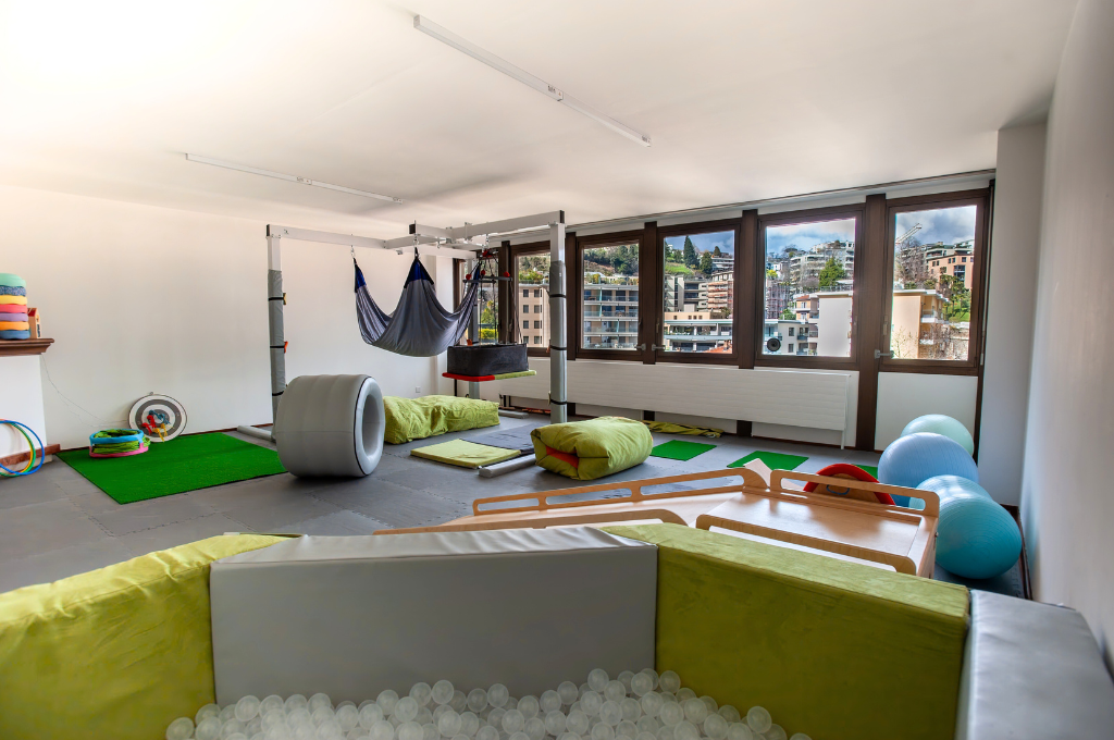 Sala luminosa con attrezzature e giochi per attività motorie e riabilitative pediatriche.
