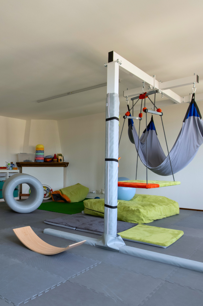 Stanza attrezzata con giochi e strutture per attività motorie e riabilitative pediatriche.