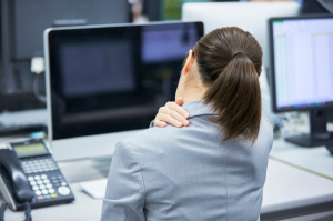 Donna in ufficio seduta alla scrivania che si massaggia la spalla davanti al computer.