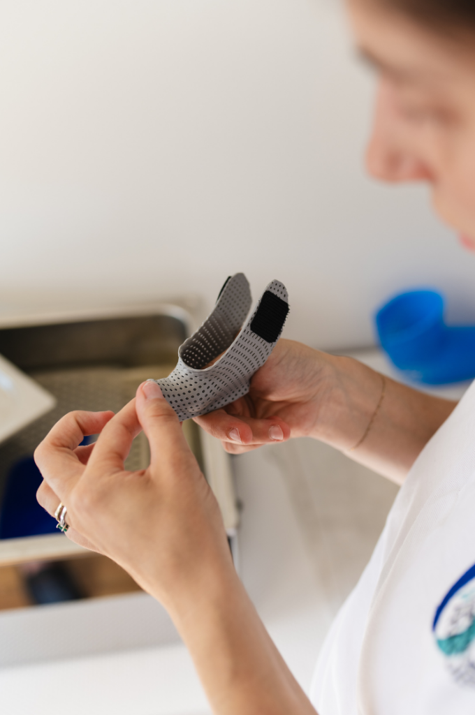 ChatGPT ha detto: Operatrice sanitaria che rifinisce un tutore ortopedico traforato per le dita della mano.